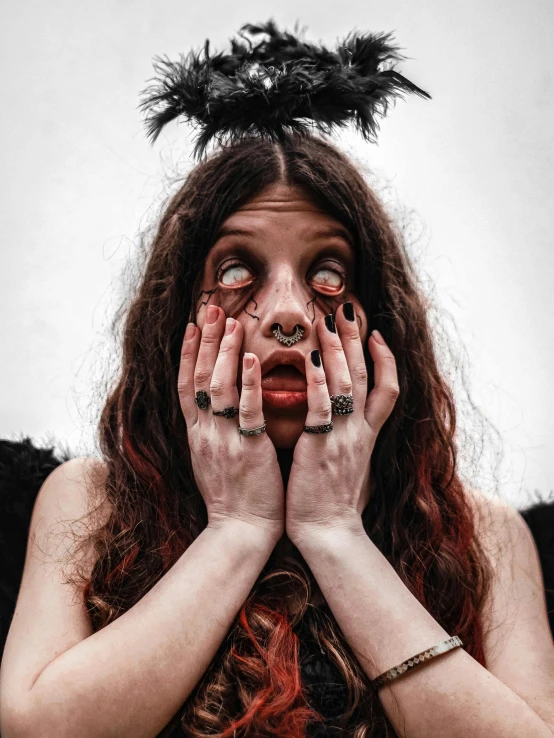 woman with red cheeks, wearing black and white makeup and holding her hands to her face while covering both hands