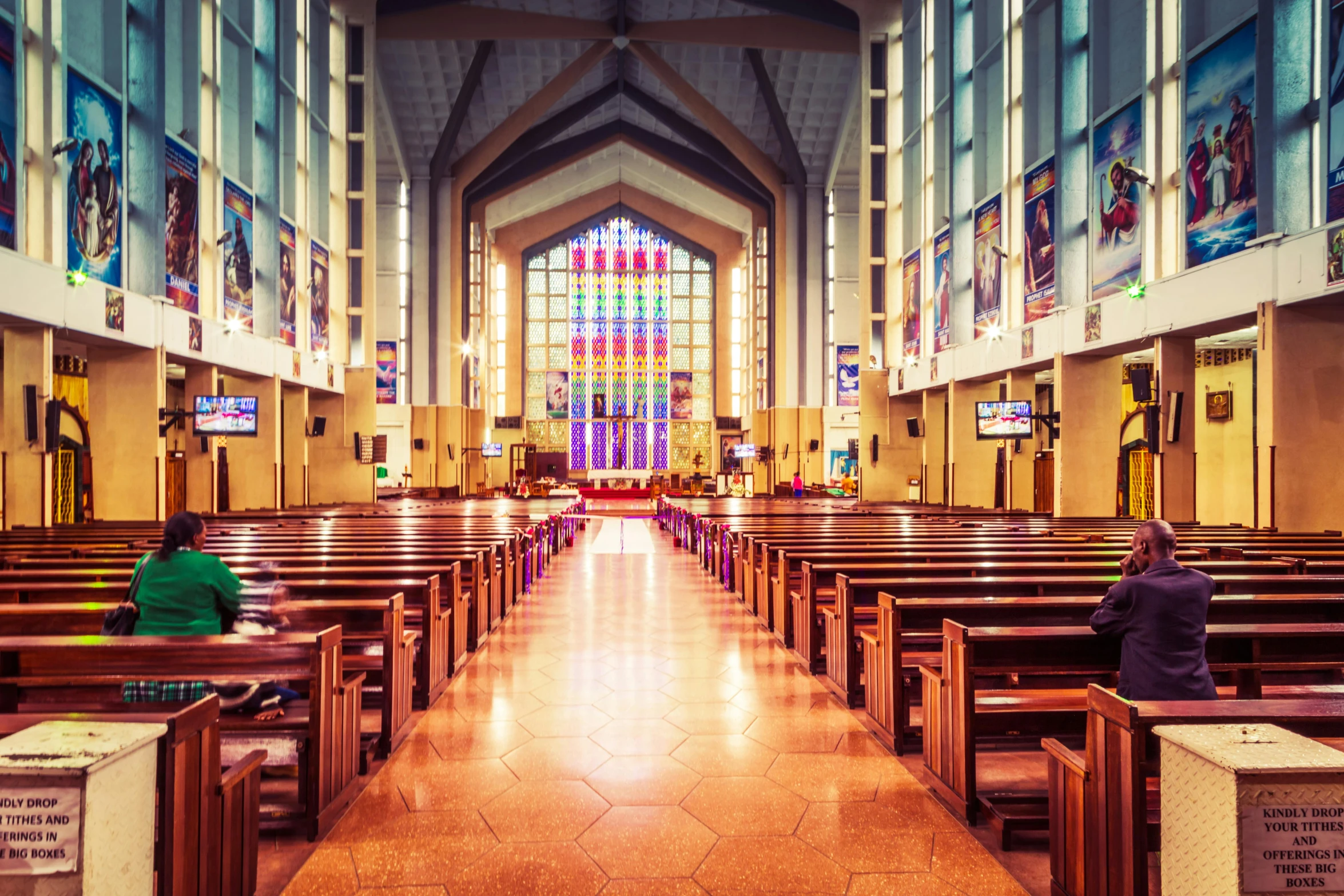 two people sitting at pews in front of stained glass windows