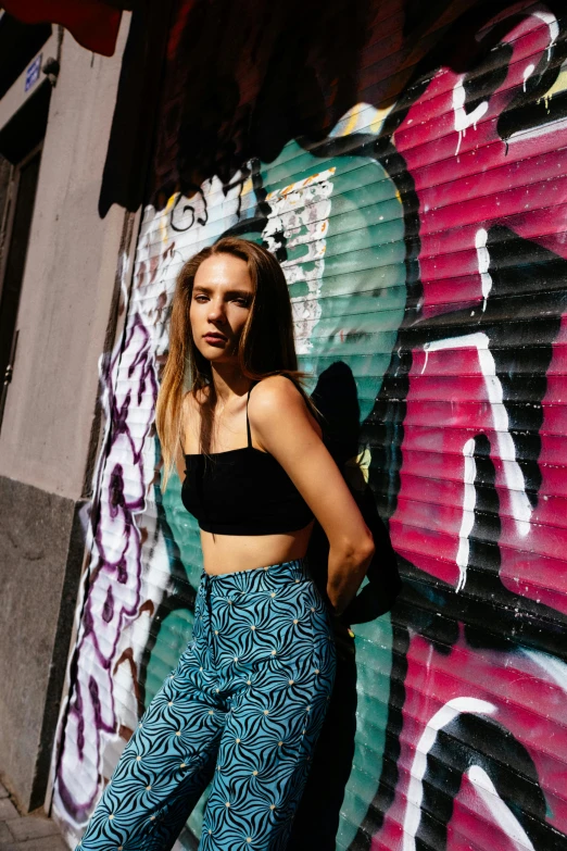 a girl wearing crop tops and high waisted pants standing in front of graffiti on a wall