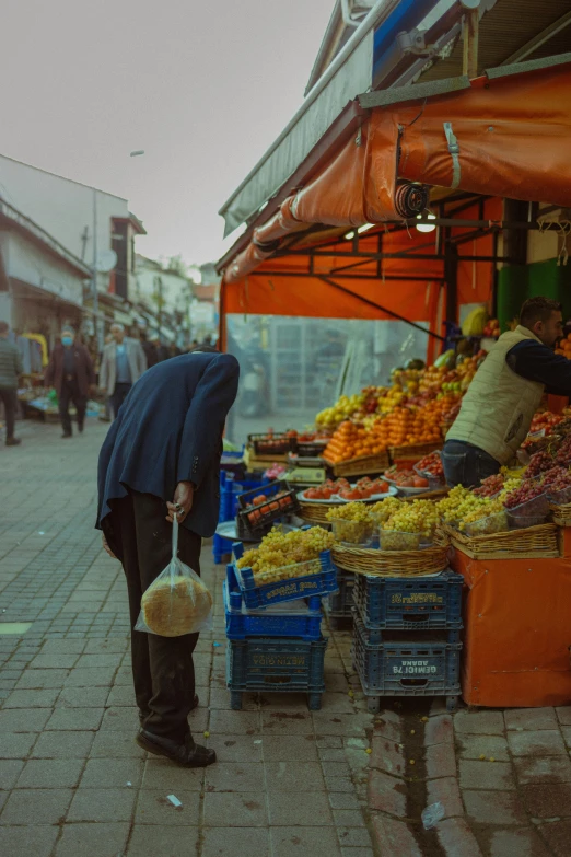 the man stands in the alley between the fruit stand and his cart