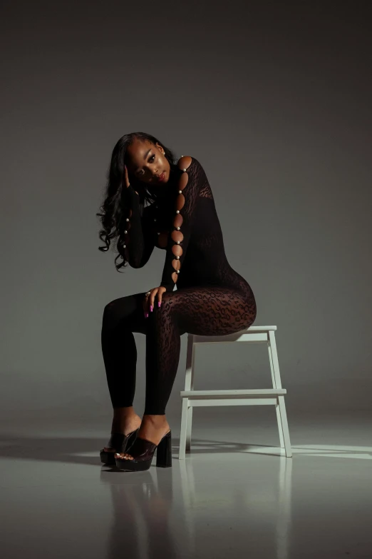 a young woman sitting on a stool wearing all black clothing