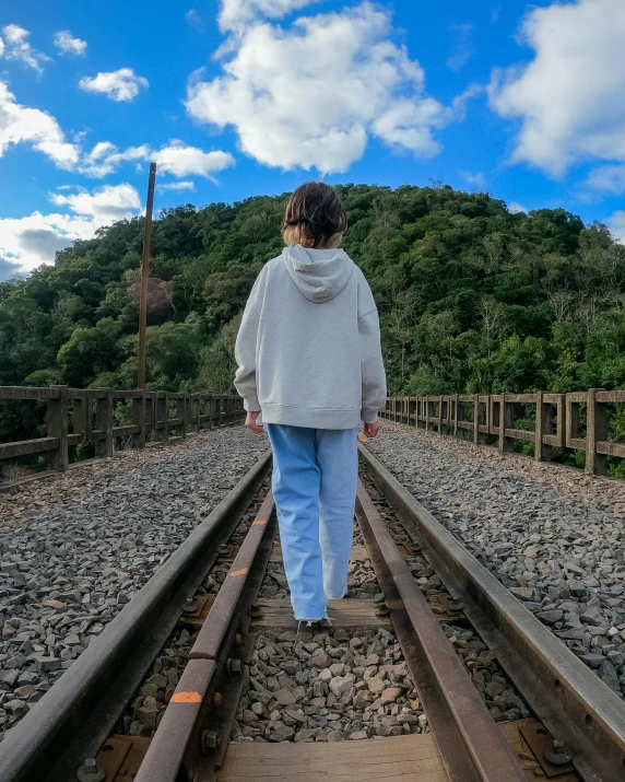 the woman walks on railroad tracks towards a forested hill