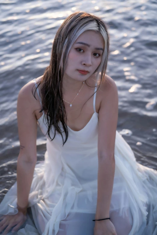 a woman sits in the water wearing a white dress