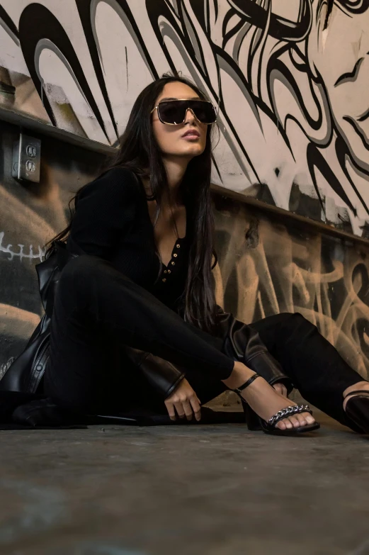woman in glasses sitting in front of a graffiti covered wall