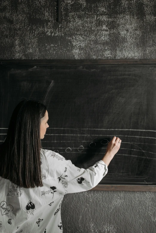 a woman writes on a blackboard while leaning against it