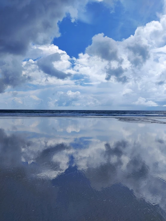 a beach with waves and clouds reflected in water