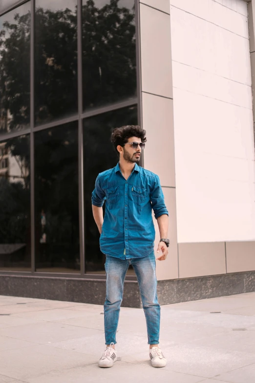 a man standing outside wearing blue denim with a white t - shirt