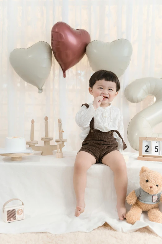 a baby sits on top of a blanket in front of balloon hearts