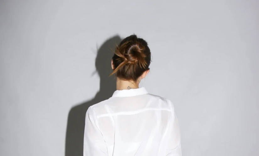 back view of a person standing against a wall wearing white blouse and pants