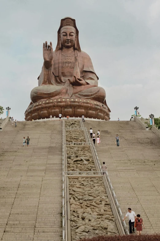 people walk up a steps leading to a large buddha statue