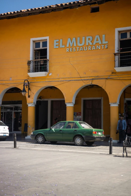 a street scene with focus on the green car parked outside a restaurant