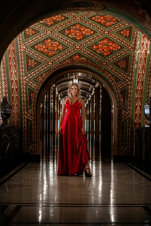 the woman in a red dress is walking through an ornate archway