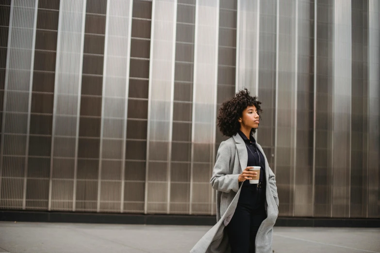 a woman walking down a city street with her coffee