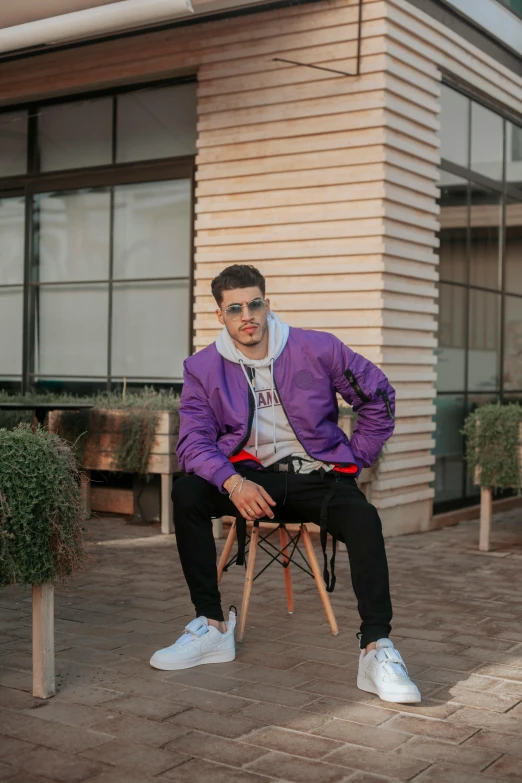 man sitting on chair with sunglasses on his face, dressed in a purple jacket