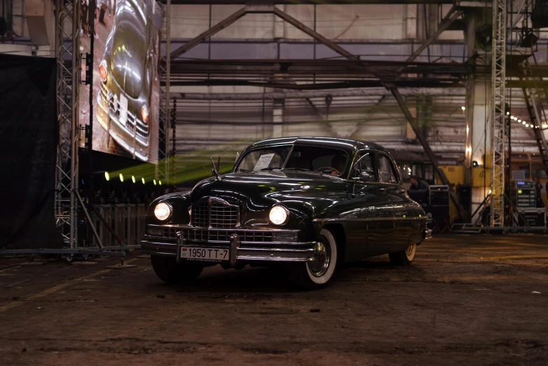 a vintage car is parked in front of a large screen at night