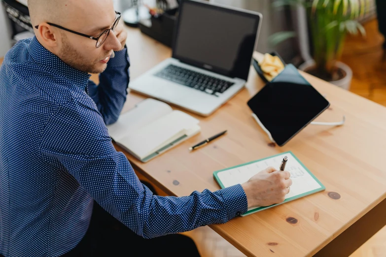 man in a blue shirt writing on clipboard at a wooden table