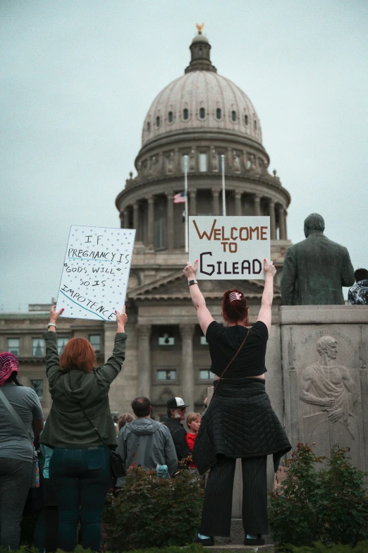 two woman hold up signs in front of a state building