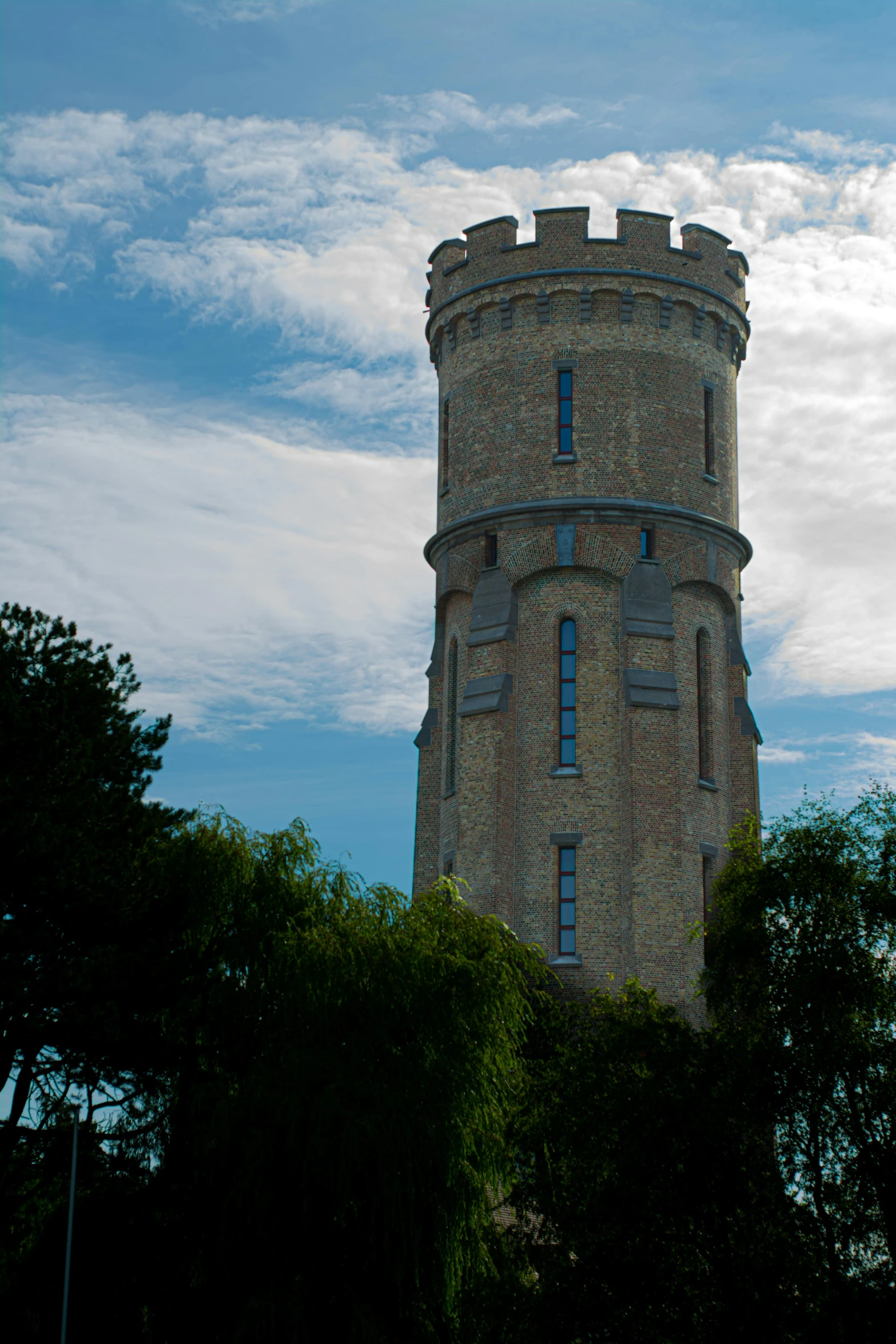 a brick clock tower in a sunny day with trees around