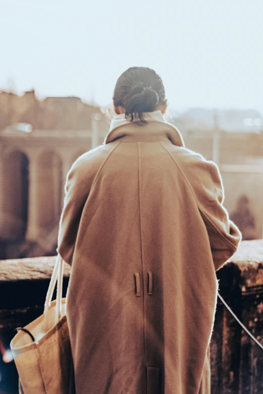 a woman in a brown coat holding a tan bag