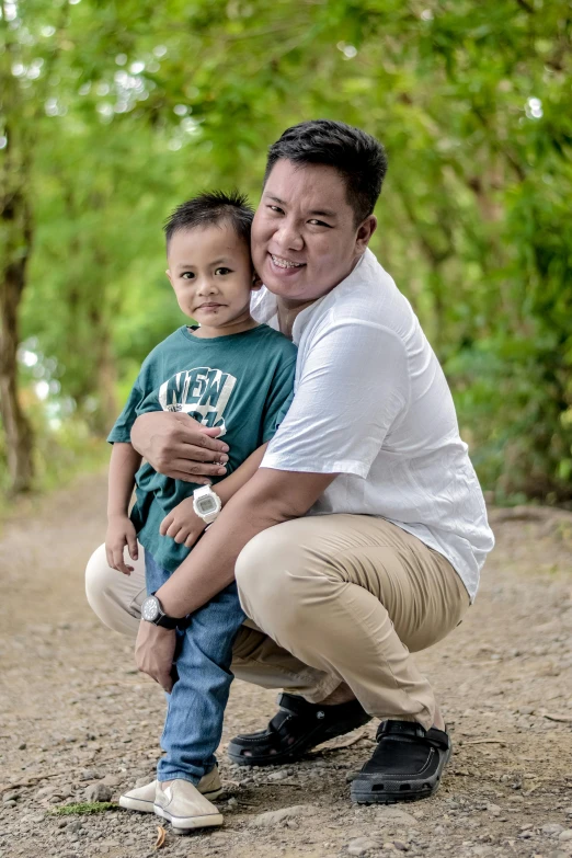 a man holds a small child as he squats in a park