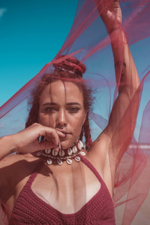 woman in a red  top leaning against her face wearing pearls and netting