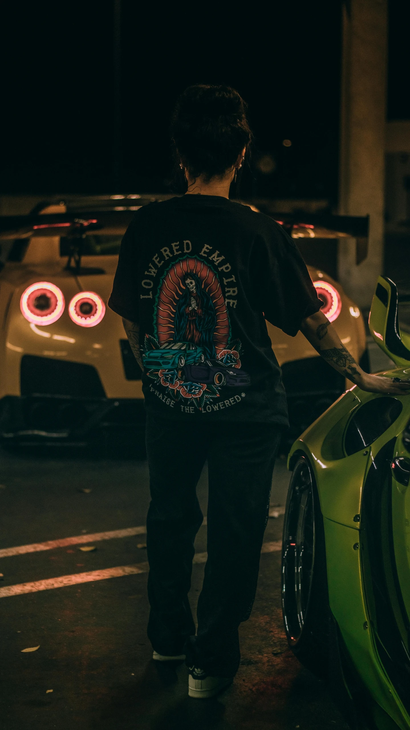 a man standing near some cars and a neon sign