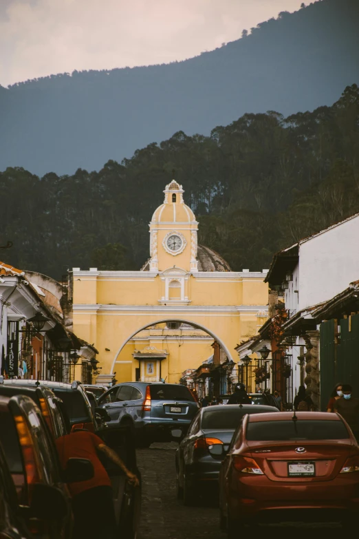 a yellow clock tower rises high above a road with a mountain in the background