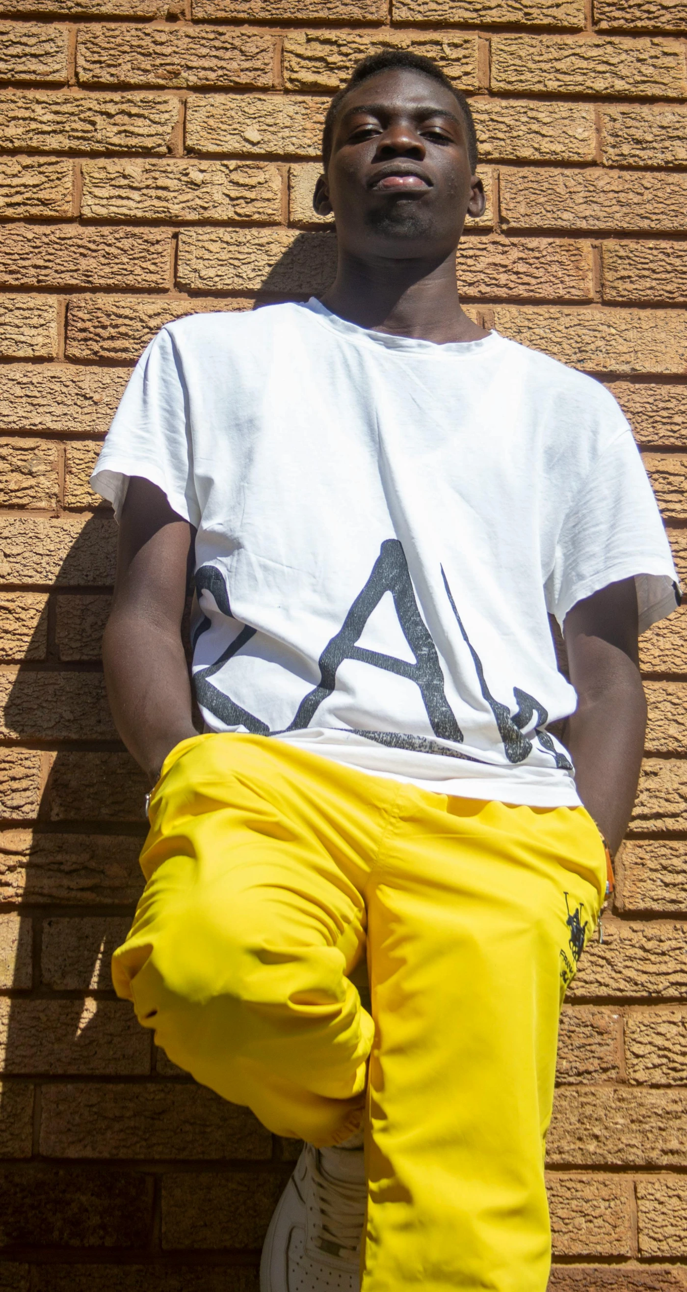 a man in yellow pants is standing against a wall