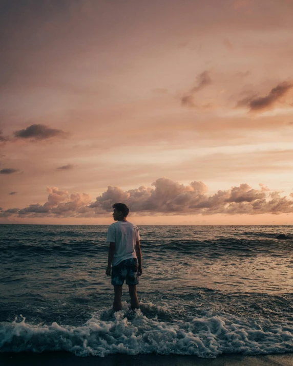 a man standing in the ocean watching the sun go down