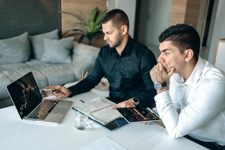 two men sit at a white table and look over paperwork