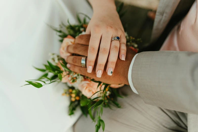 hands hold hands next to each other, with a bouquet behind them