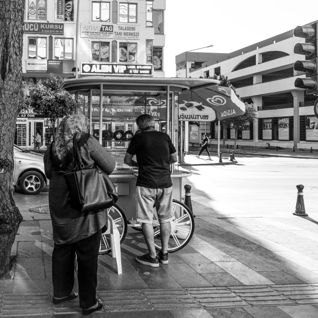 a man and woman on a street corner looking at the sidewalk