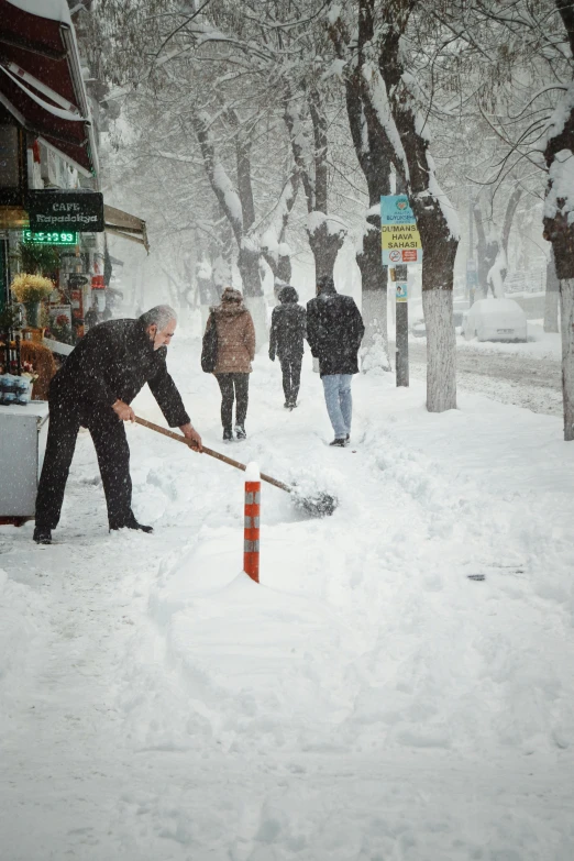 a man shovels snow from his street as a group of people walk past