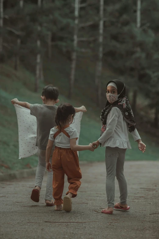 two young children hold hands walking down a gravel road