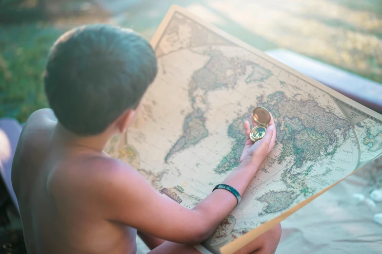 a boy in swimsuit holds an open world map with his hands