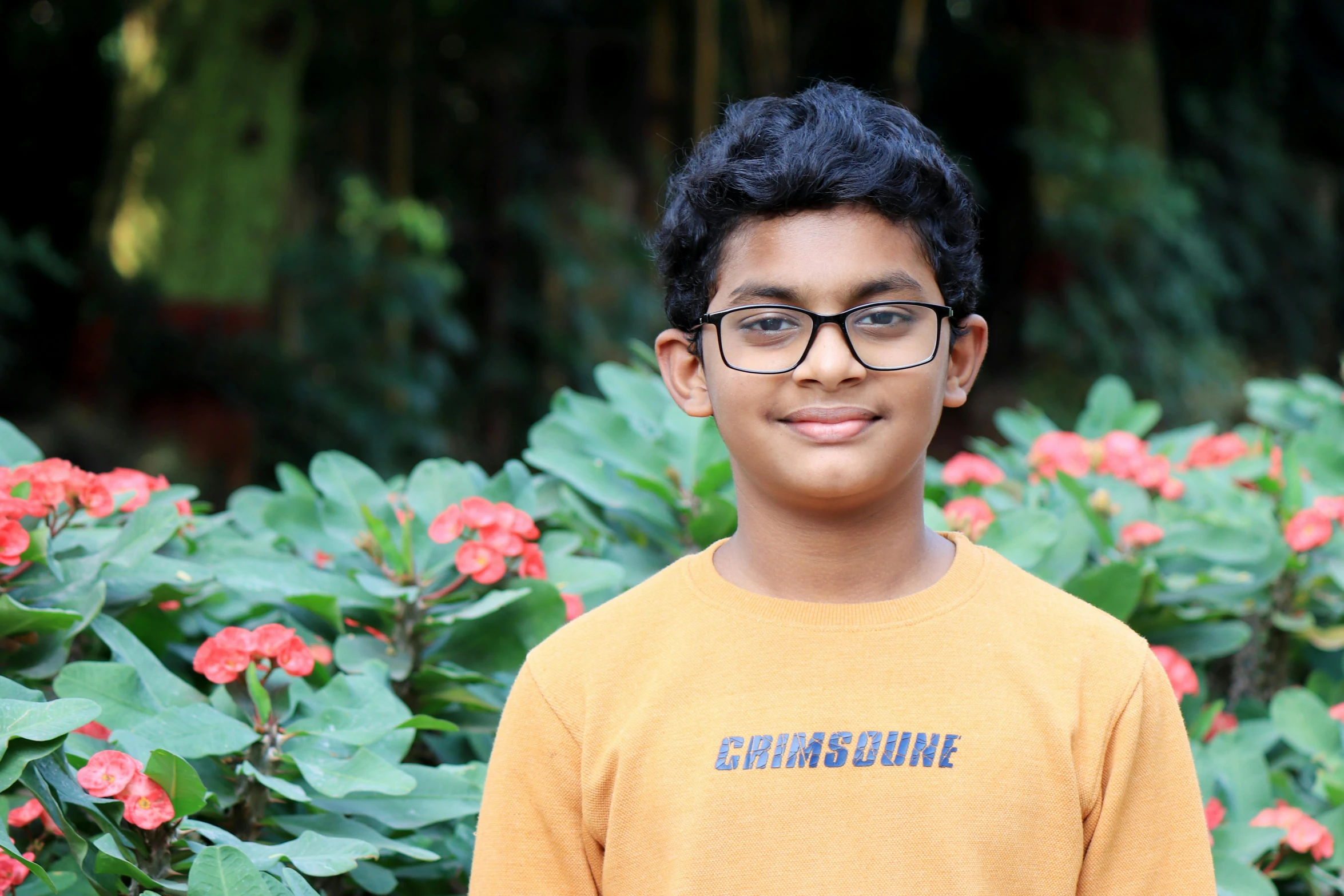 a  with glasses standing in front of red flowers