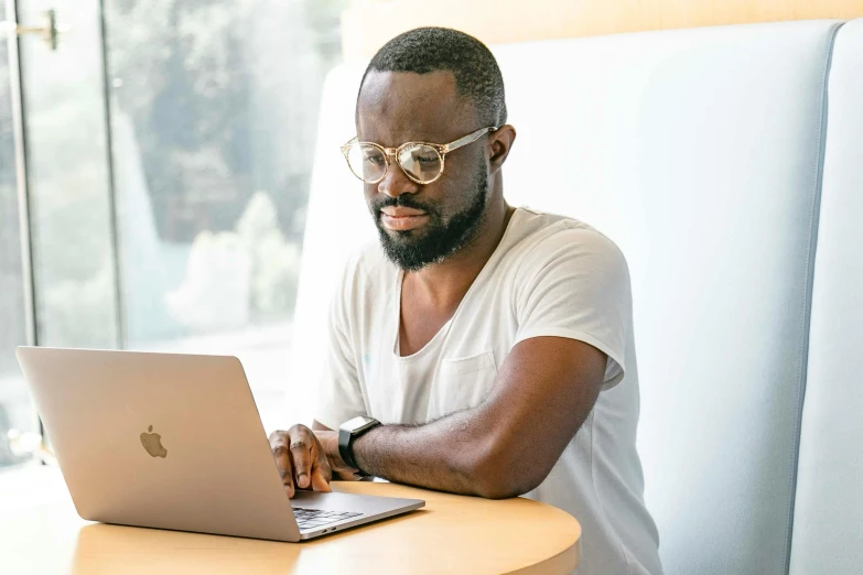 a person wearing glasses on a table looking at an open laptop