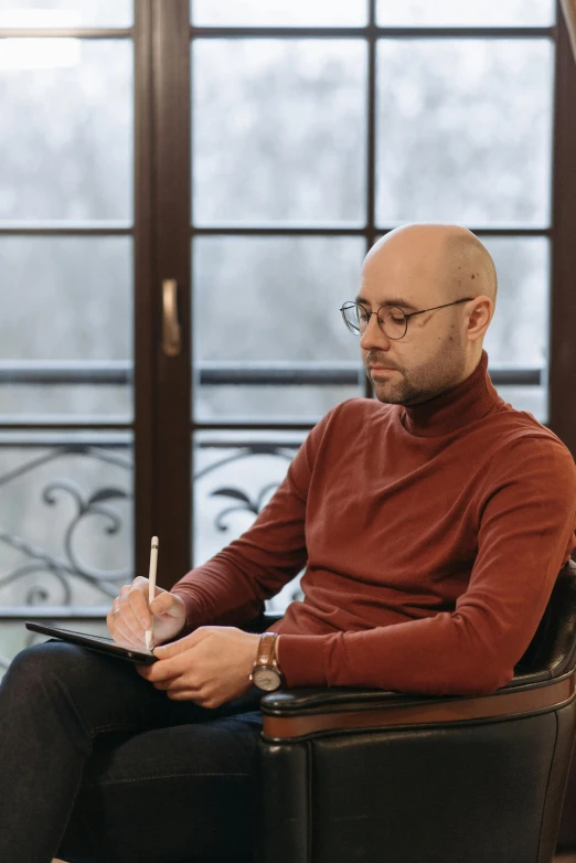 a man wearing glasses sitting in a chair writing