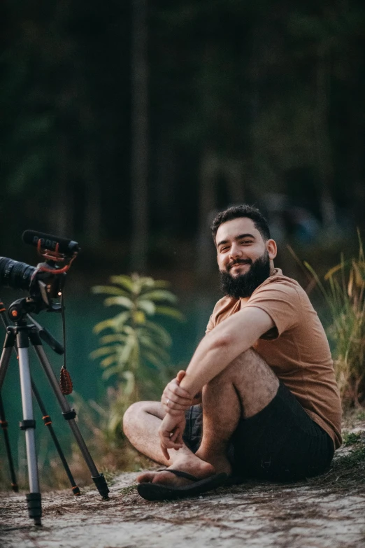 a man sitting on the ground next to a telescope