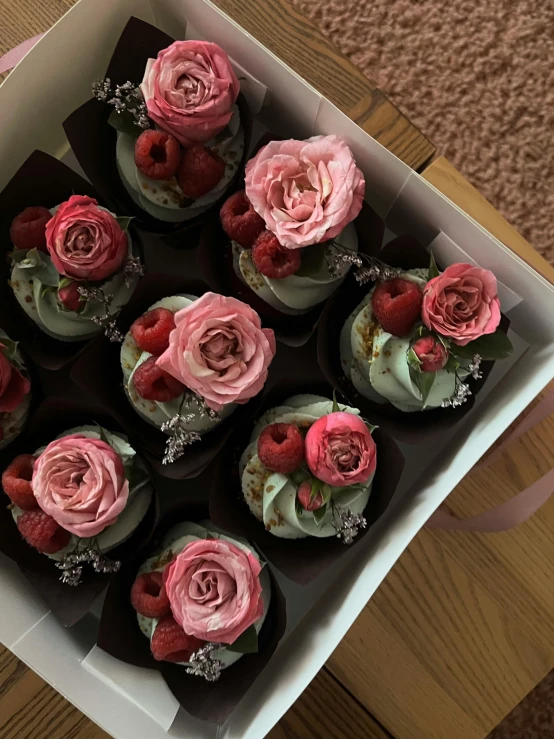 box with cupcakes decorated in pink flowers on a table