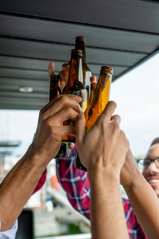 several people hold beer bottles and raise their hands high