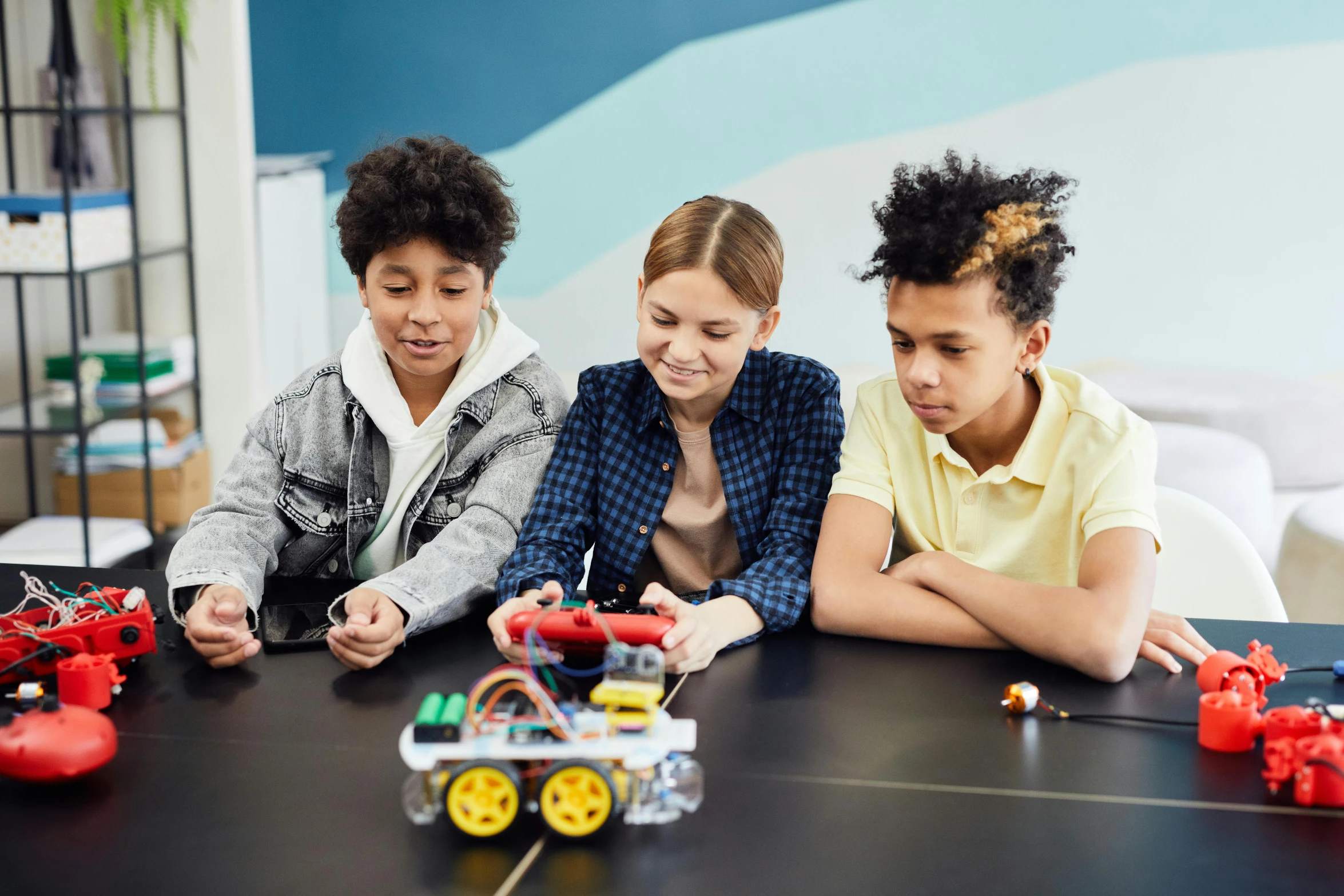 three children at a table together playing with a robot