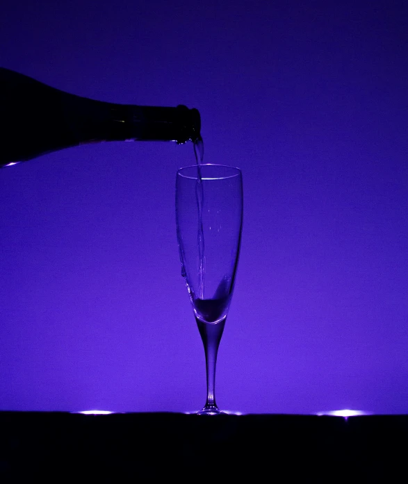 someone pouring champagne into a glass in front of purple backdrop