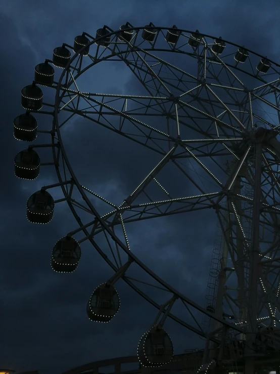 a ferris wheel illuminated at night under cloudy skies