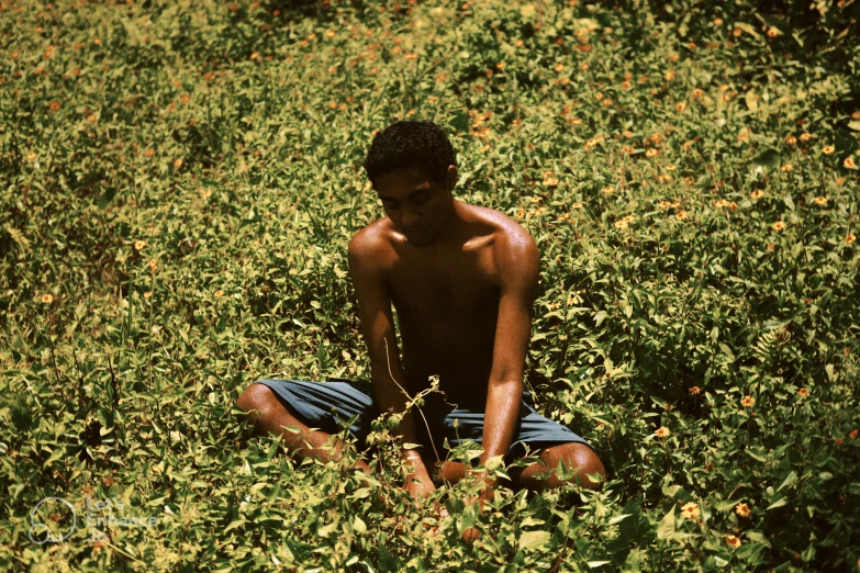 young man sitting in grass in front of flower bush