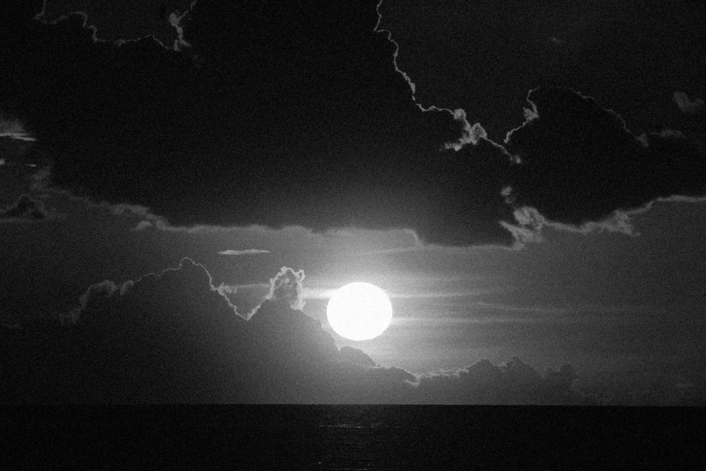 full moon in black and white, clouds over the water