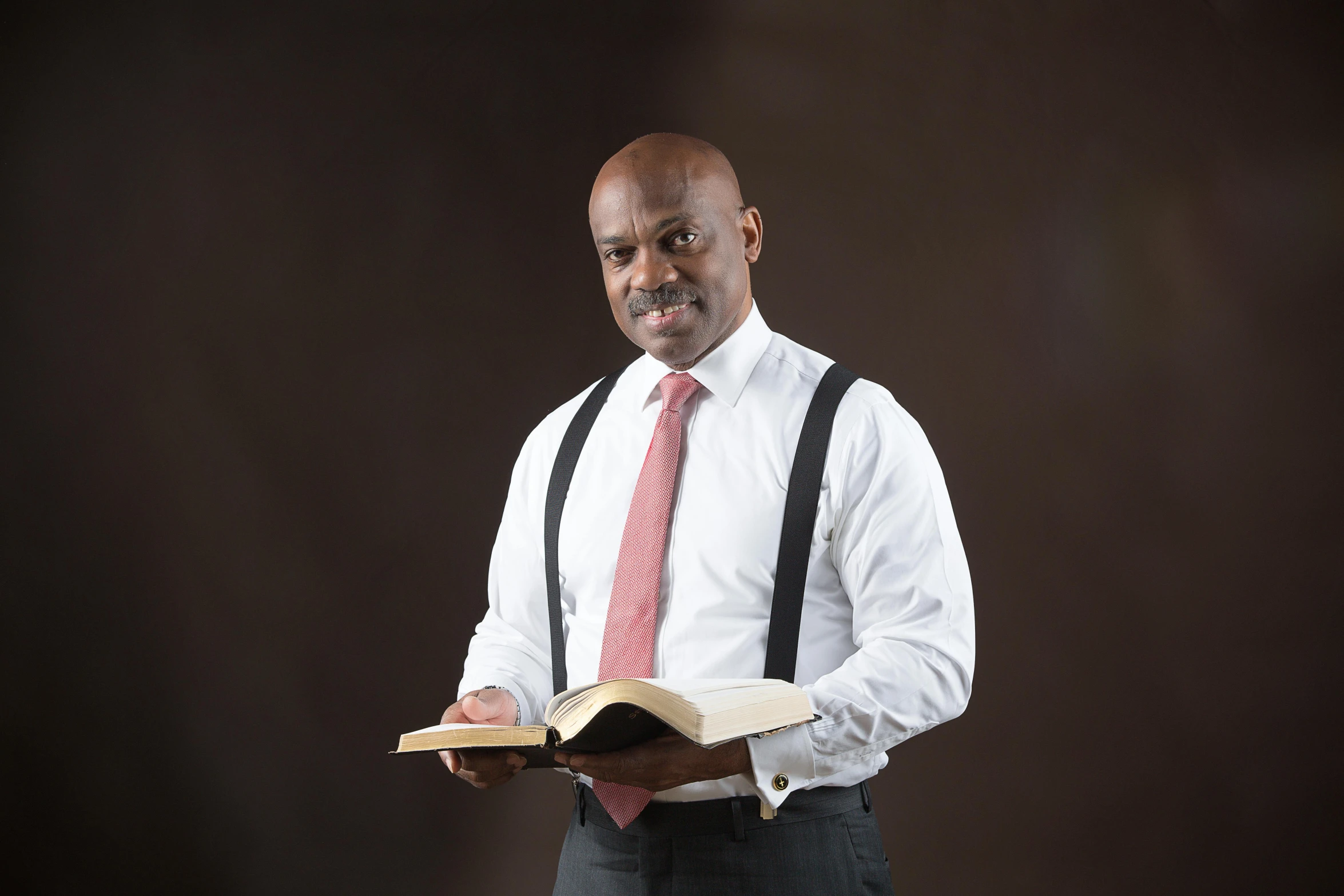 man in white shirt and black suspenders holding a book