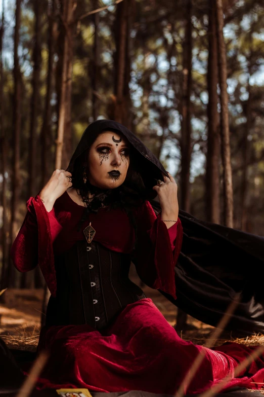 a woman in red dress sitting down with black makeup on her face