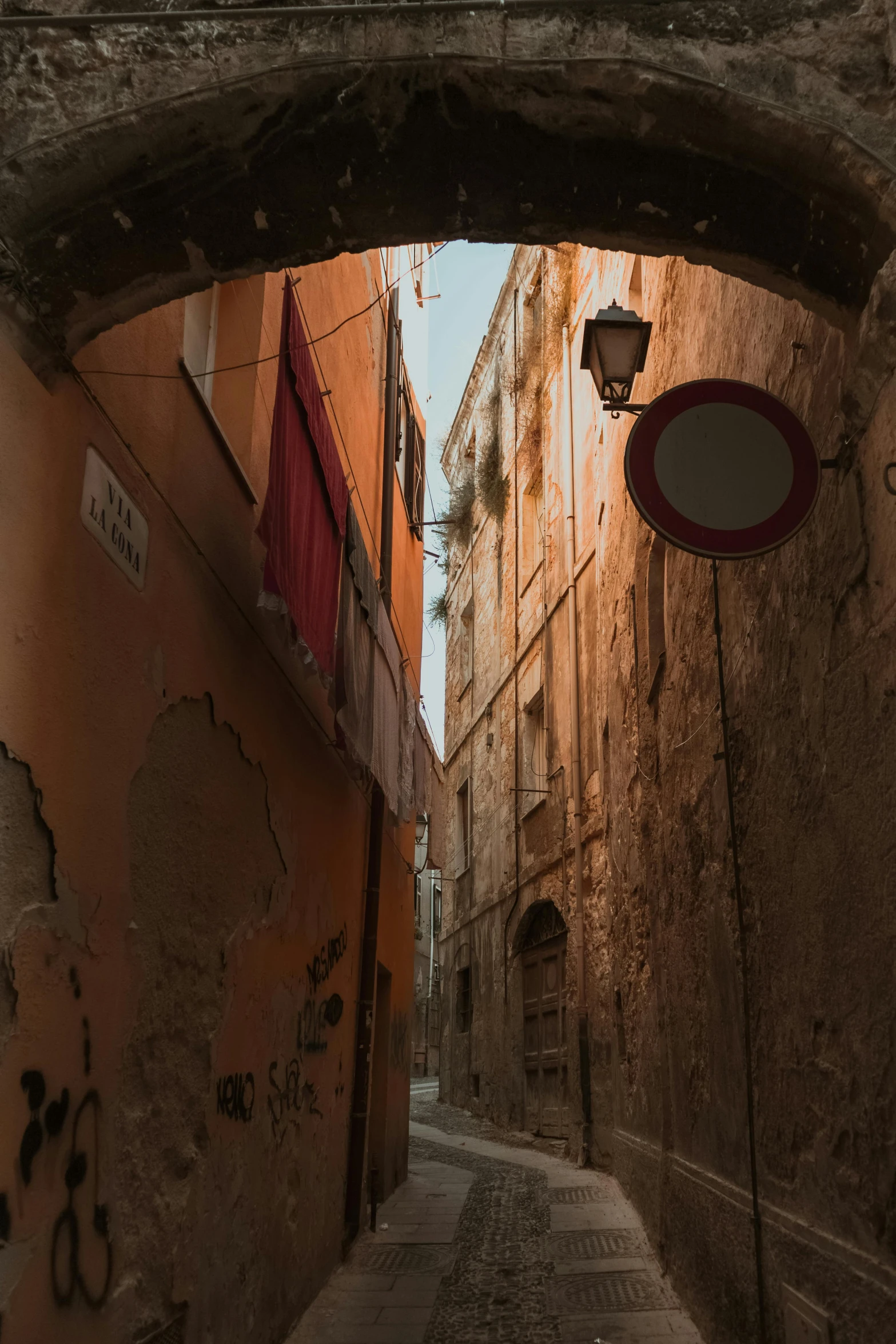 a narrow city street that has graffiti on the walls and is under an arch