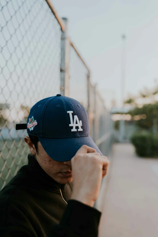 a man leans against a fence while wearing a baseball cap